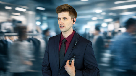 A calm retail manager standing in a chaotic store, using the Motorola TLK 25 wearable radio to maintain operational silence and reduce staff burnout.